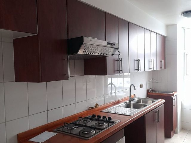 Cocina con campana extractora y muebles superiores de madera oscura, departamento en Edificio Punta Cavancha, Iquique
