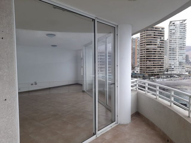 Living vacío con salida al balcón y vista a edificios costeros, departamento en Edificio Punta Cavancha, Iquique