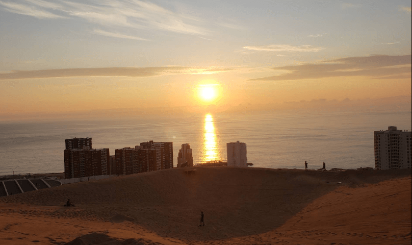 Atardecer visto desde duna cercana, con vista a edificios costeros de Iquique
