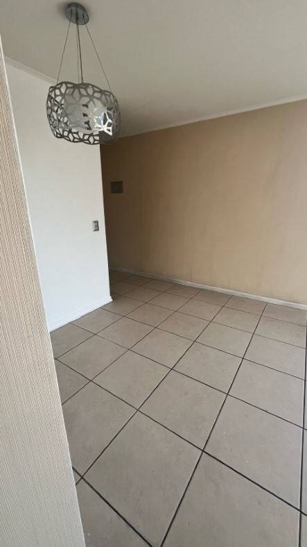 Comedor vacío con lámpara decorativa y piso cerámico, departamento Puesta de Sol, Iquique