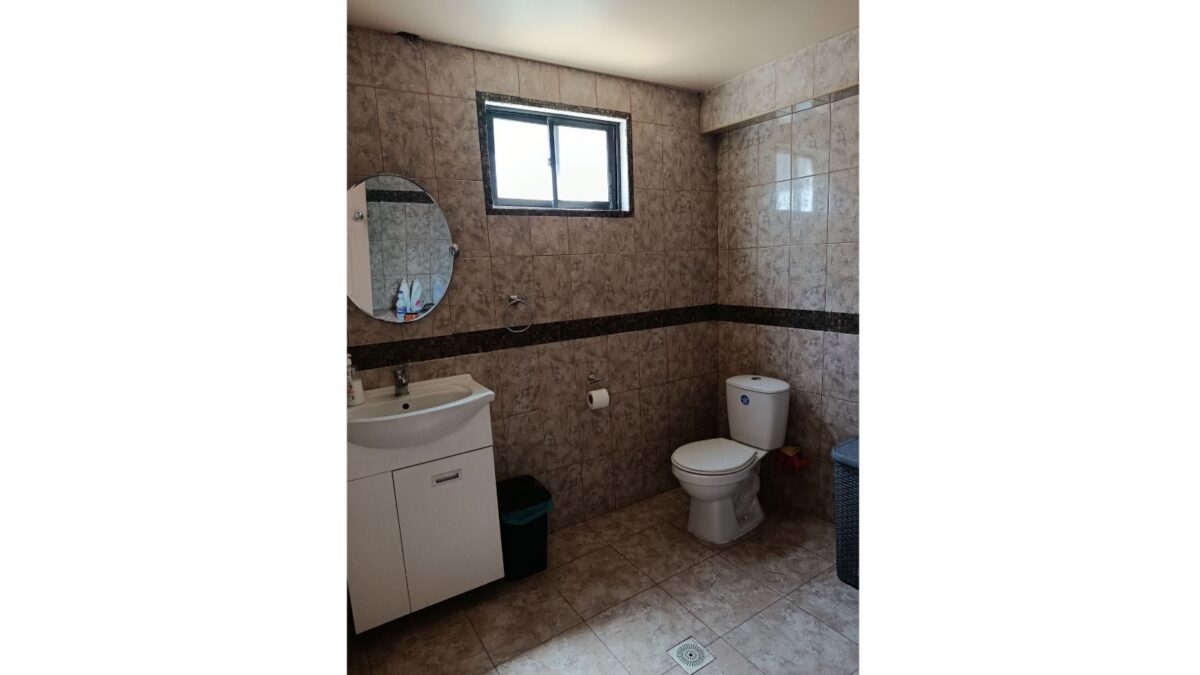 Baño con espejo redondo y ventana, casa en venta en Alto Hospicio