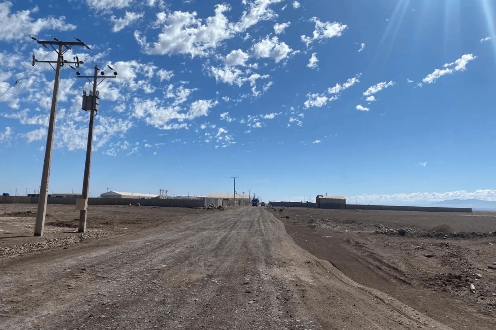 Camino de tierra con postes eléctricos y bodegas industriales al fondo, terreno en Pozo Almonte