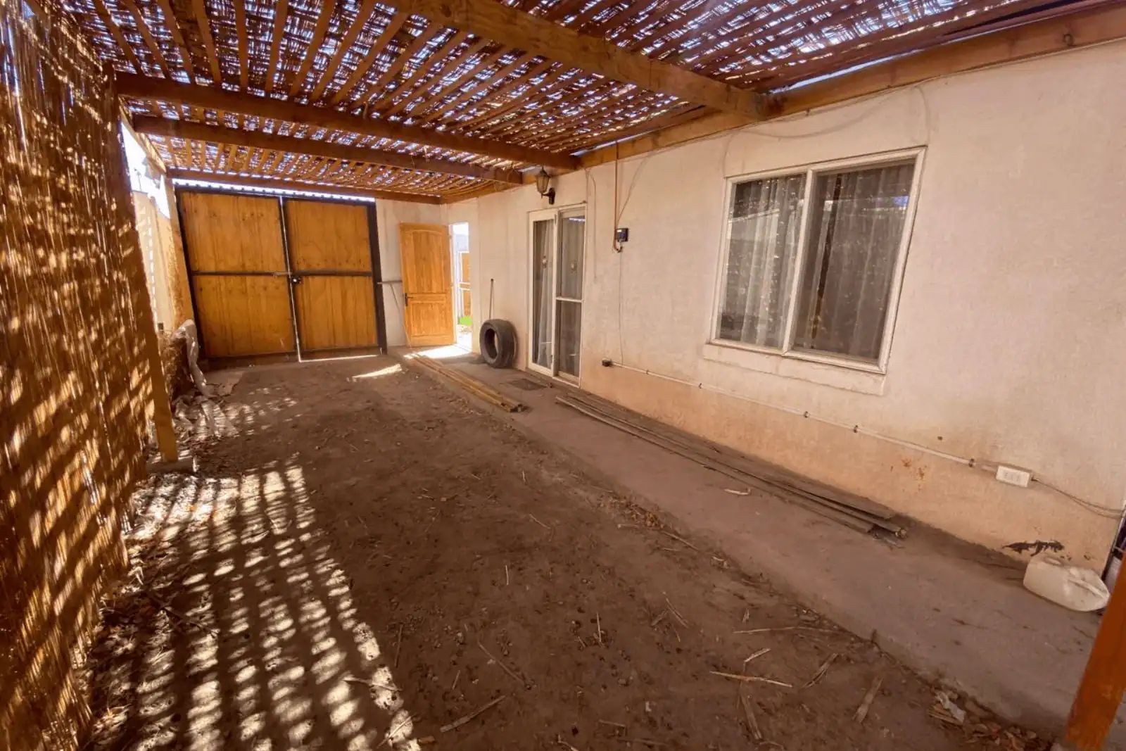 Patio techado lateral con acceso a puerta corrediza y ventanas de la casa