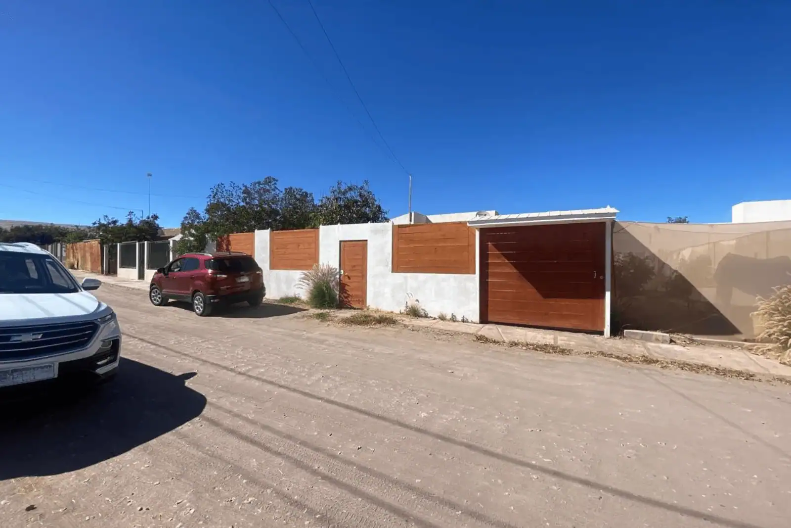 Vista exterior de la calle frente a la casa, con muro perimetral de albañilería y madera