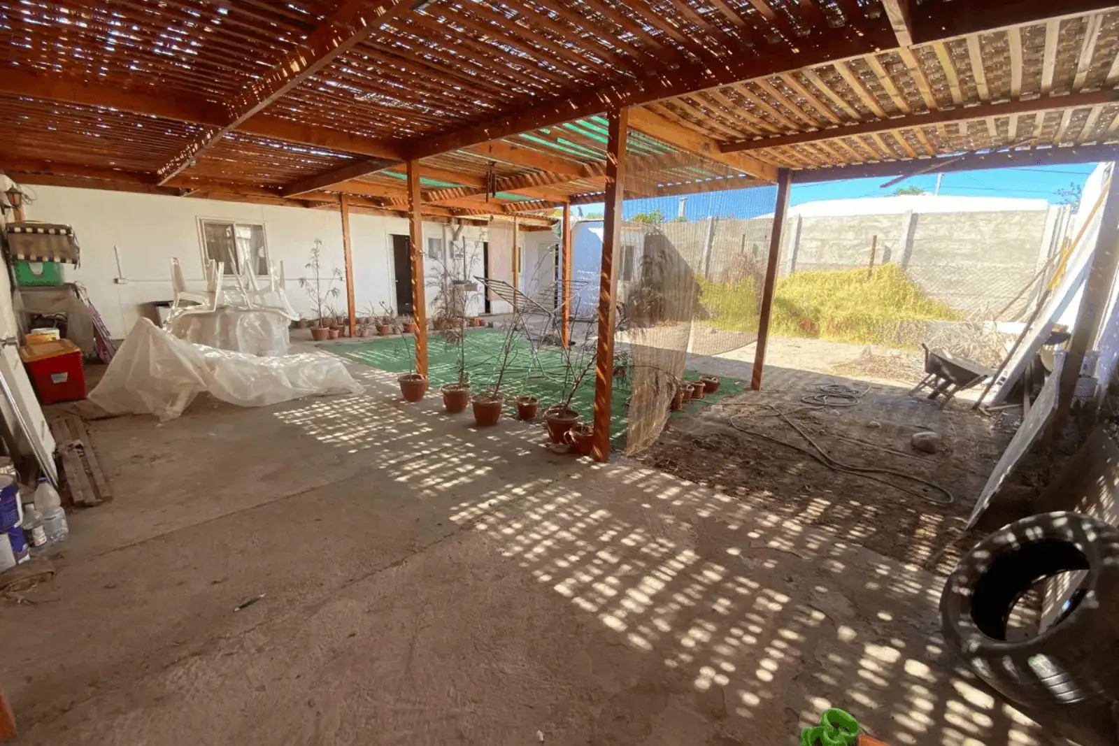 Patio techado con malla sombra, macetas y acceso a muro perimetral